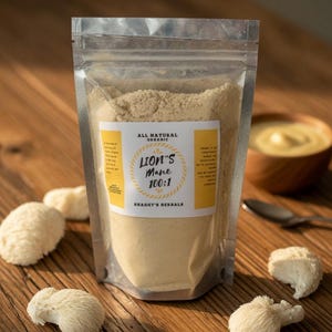 May include: A clear, resealable pouch filled with light brown powder labeled "Lion's Mane 100:1" by Shaggy's Herbals. Several white, textured lion's mane mushrooms are scattered on a wooden surface. A small wooden bowl and spoon are in the background.