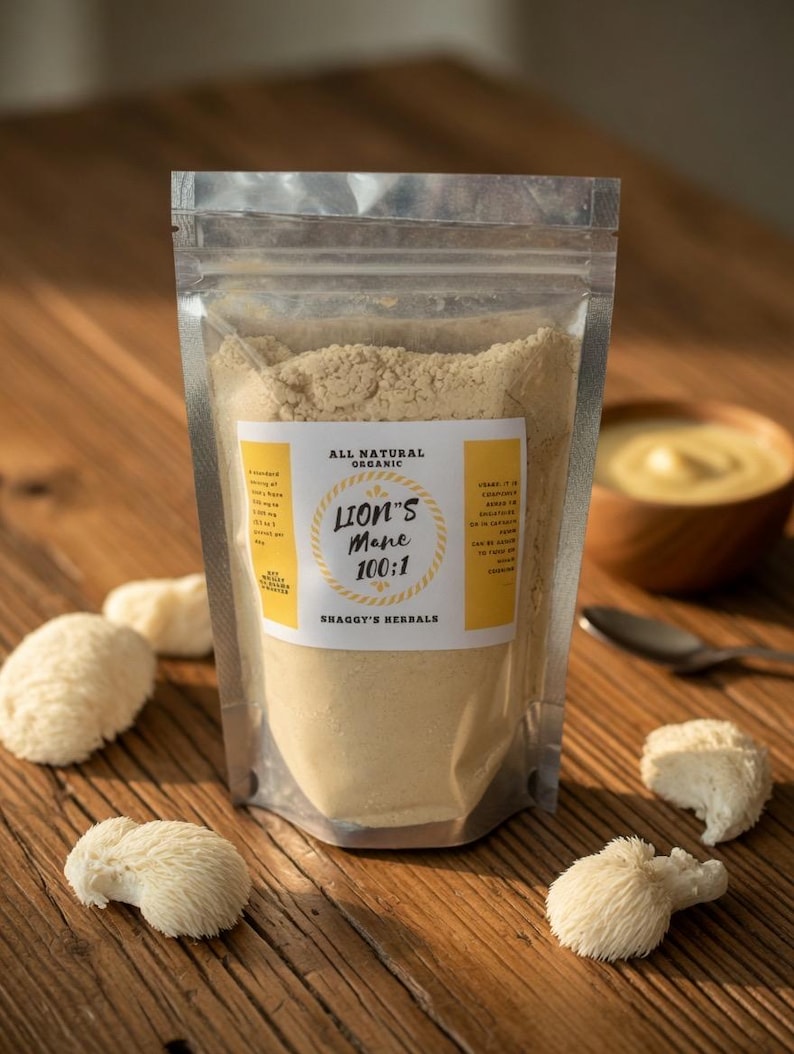 May include: A clear, resealable pouch filled with light brown powder labeled "Lion's Mane 100:1" by Shaggy's Herbals. Several white, textured lion's mane mushrooms are scattered on a wooden surface. A small wooden bowl and spoon are in the background.