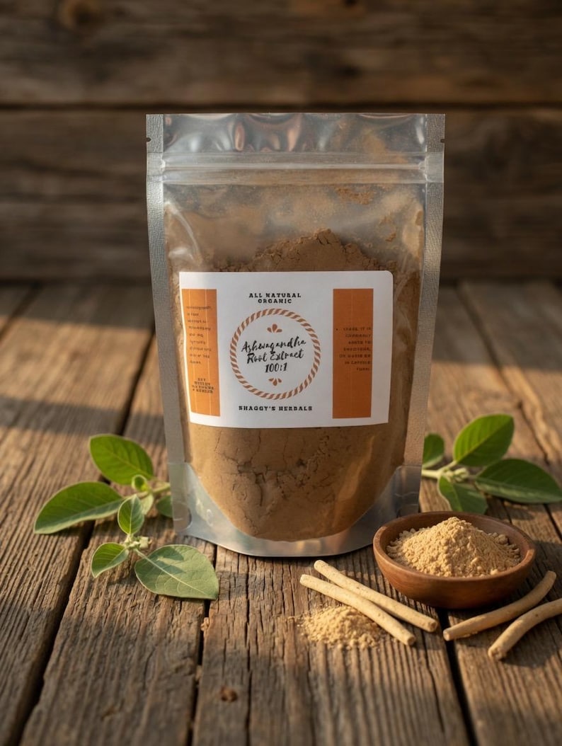 May include: A clear, resealable bag filled with brown powder labeled "Ashwagandha Root Extract 100:1" sits on a wooden surface. A small wooden bowl and several sticks of ashwagandha are also present. Green leaves are arranged around the bag and bowl.