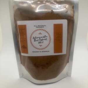 May include: A silver, resealable pouch filled with brown powder. The label reads "Ashwagandha Root Extract 100:1" with "All Natural Organic" at the top and "Shaggy's Herbals" at the bottom. The label has orange accents.