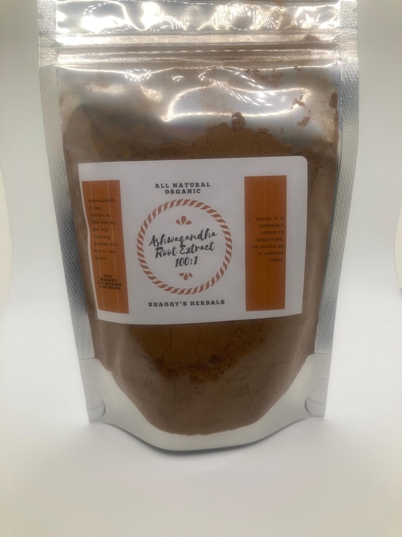 May include: A silver, resealable pouch filled with brown powder. The label reads "Ashwagandha Root Extract 100:1" with "All Natural Organic" at the top and "Shaggy's Herbals" at the bottom. The label has orange accents.