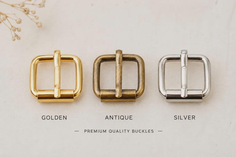 May include: Three square metal buckles arranged in a row, featuring a shiny golden finish, a matte antique brass finish, and a polished silver finish. The text below the buckles reads GOLDEN, ANTIQUE, SILVER, and PREMIUM QUALITY BUCKLES.