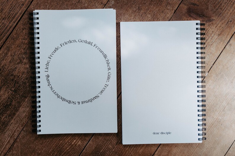 K&ouml;nnte beinhalten: Zwei spiralgebundene Notizb&uuml;cher, eines mit einem hellblauen Umschlag und dem Text "Sanftmut & Selbstbeherrschung. Liebe, Freude, Frieden, Geduld, Freundlichkeit, G&uuml;te, Treue" in einem Kreis um die Mitte, und das andere mit einem hellblauen Umschlag und dem Text "dear disciple" unten.