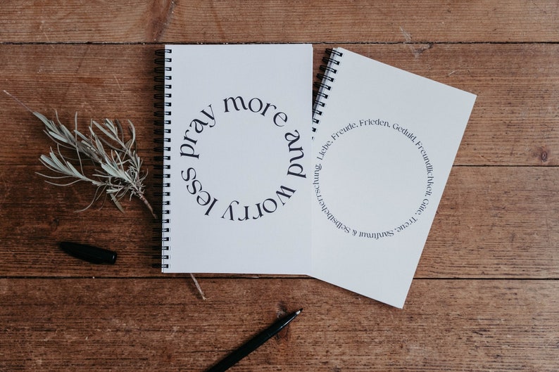 K&ouml;nnte beinhalten: Zwei wei&szlig;e Spiralblock-Notizb&uuml;cher mit schwarzem Text. Das Notizbuch links hat den Text "worry less pray more". Das Notizbuch rechts hat den Text "Treue, Satmar & Selbstbeherrschung, Liebe, Freude, Frieden, Geduld, Freundlichkeit, Gnade".