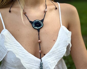 Puede incluir: Un collar largo de varias capas con un gran colgante redondo de ágata azul y blanco. El collar está hecho de cordón negro y tiene pequeñas cuentas rosas.
