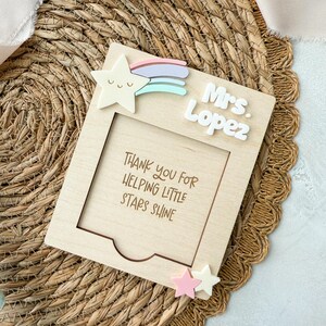 May include: Wooden frame with a rainbow and star design. The frame has a cutout for a photo and the text "Thank you for helping little stars shine". The frame also has the text "Mrs. Lopez" on it.
