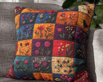 May include: Square throw pillow with a patchwork design featuring embroidered floral patterns in various colors. The pillow has a quilted texture and is placed on a gray sofa. The color palette includes shades of blue, orange, red, and purple.