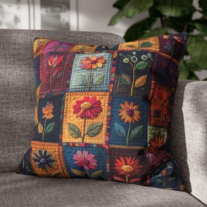 Op de afbeelding: Vierkant kussen met een patchwork ontwerp met geborduurde bloemen in verschillende kleuren. Het kussen heeft een donkere achtergrond met oranje, blauwe en rode vierkanten. De bloemen omvatten madeliefjes, tulpen en andere bloemmotieven.