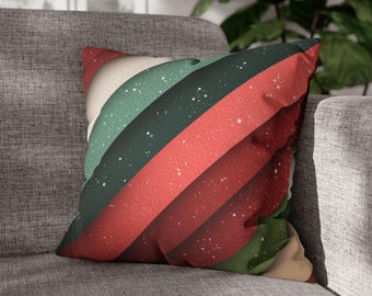 Pode incluir: Almofada decorativa quadrada com um padrão de listras diagonais em vermelho, verde e branco sujo. As listras têm uma aparência texturizada e são acentuadas com pequenos pontos brancos, criando um visual festivo. A almofada está colocada em um sofá cinza.