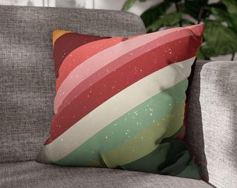 Pode incluir: Almofada quadrada com design retrô. A almofada apresenta listras diagonais em tons de vermelho, rosa, verde e branco, com uma textura salpicada. A almofada está colocada em um sofá cinza.