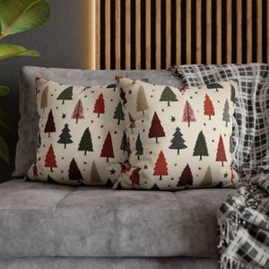 May include: Two decorative throw pillows with a cream background and a repeating pattern of Christmas trees in red, green, and brown. Small black stars are scattered between the trees. The pillows are on a gray sofa.