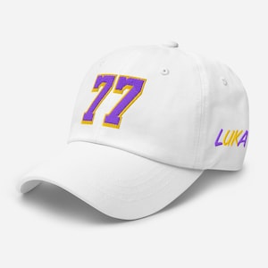 May include: White baseball cap with a purple and yellow embroidered number 77 on the front and the word "LUKA" in purple and yellow on the side.