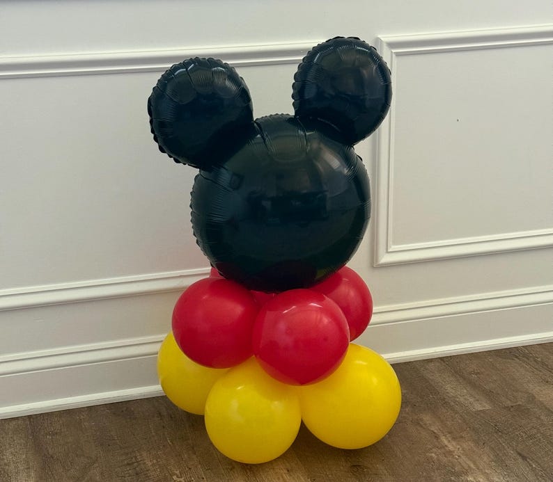 Pu&ograve; includere: Un'arrangiamento di palloncini a forma di testa di Topolino. La testa &egrave; nera, con due grandi orecchie rotonde. La base &egrave; composta da palloncini rossi e gialli, creando un'esposizione festosa.