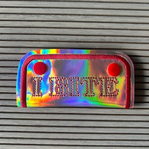 May include: A holographic iridescent patch with a red border and red button accents. The patch has the word "I BITE" embroidered in red thread.