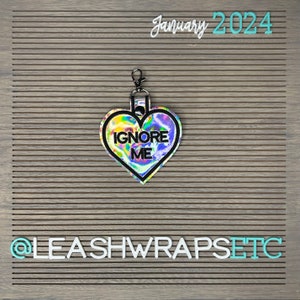 May include: A holographic heart-shaped keychain with a black border and the text "IGNORE ME" in black lettering. The keychain is attached to a silver metal ring.