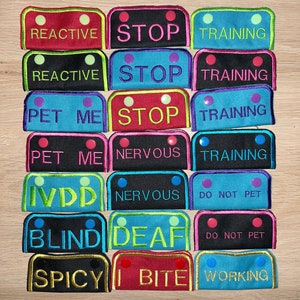 May include: A set of 12 colorful dog training patches with various text, including "Reactive", "Stop", "Training", "Pet Me", "Nervous", "IVDD", "Blind", "Deaf", "Do Not Pet", "Spicy", "Bite", and "Working".