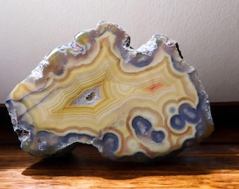 May include: A large, polished agate slice with a variety of colors, including yellow, orange, red, and blue. The agate has a natural, organic shape and a smooth, polished surface.