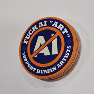 May include: A stack of round stickers with an orange border and a blue center. The stickers have the text "FUCK AI 'ART'" and "SUPPORT HUMAN ARTISTS" around a white "AI" symbol with a red slash through it.
