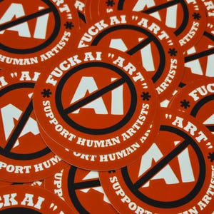 May include: A collection of orange stickers with black and white text. The stickers have a circular design with the words "FUCK AI 'ART'" and "SUPPORT HUMAN ARTISTS". The AI symbol is crossed out.