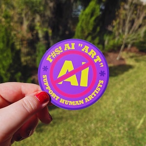 May include: A round purple sticker with yellow and pink text and graphics. The sticker reads "F#! AI "ART"" with a red slash through the word "AI". The text "SUPPORT HUMAN ARTISTS" is also on the sticker.