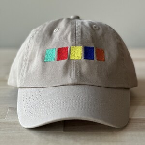 May include: A beige baseball cap with a row of five embroidered squares in turquoise, red, yellow, blue, and orange.