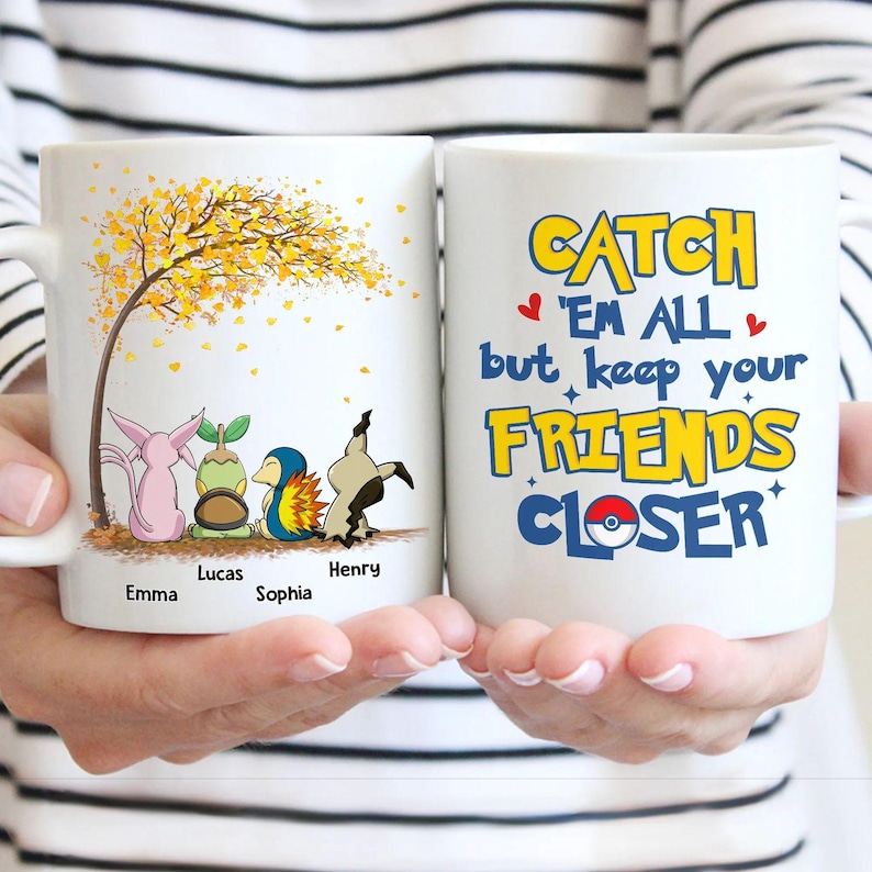 May include: Two white ceramic mugs. One mug features cartoon characters under a tree with yellow leaves and names. The other mug has the text "Catch 'Em All but keep your FRIENDS CLOSER" in yellow and blue.