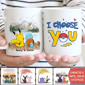 May include: Two white ceramic mugs are held in hands. One mug features Pikachu and Squirtle on a dock with a mountain backdrop, the names "Henry" and "Emma" are below. The other mug says "I Choose You" with a Pokeball design.