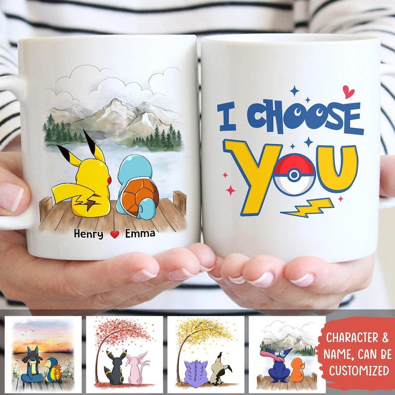 May include: Two white ceramic mugs are held in hands. One mug features Pikachu and Squirtle on a dock with a mountain backdrop, the names "Henry" and "Emma" are below. The other mug says "I Choose You" with a Pokeball design.