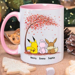 May include: White ceramic mug with a pink handle and interior. The mug features a colorful illustration of three cartoon characters under a tree with red leaves. The names "Henry", "Emma", and "Sophia" are printed below the characters.