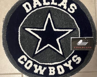 Puede incluir: Alfombra redonda con el logotipo de los Dallas Cowboys. El diseño incluye una estrella azul marino, un contorno blanco y las palabras "DALLAS COWBOYS" en letras blancas sobre un fondo gris y azul marino.