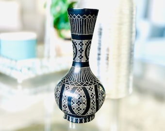 May include: A black and white patterned ceramic vase with a geometric design. The vase is sitting on a glass table.