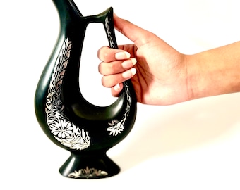 May include: A black ceramic jug with silver floral designs. The jug has a unique curved handle and a wide base.
