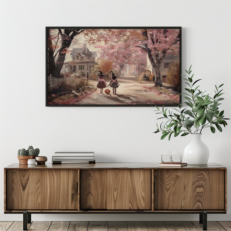 May include: Two children dressed as witches walk down a street lined with trees in autumn. They are carrying a pumpkin and wearing black hats. The street is covered in fallen leaves.