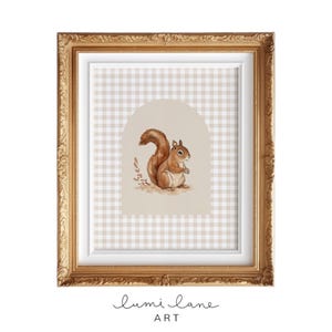 May include: A framed print of a watercolor illustration of a brown squirrel sitting on a beige and white gingham background. The frame is gold with ornate detailing.