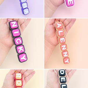 Op de afbeelding: Een collectie van zes gepersonaliseerde sleutelhangers met vierkante, kleurrijke siliconen kralen met witte reli&euml;fletters. Elke sleutelhanger toont een unieke naam: SAMANTHA, ALE, NICKY, ALENNY, ROXANA en DELEANA, bevestigd aan een kleine ketting.