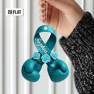 May include: A teal boxing glove ornament with a ribbon featuring the name "Sophia" and adorned with teal roses. The ribbon has a leopard print pattern. The ornament is suspended by a string.