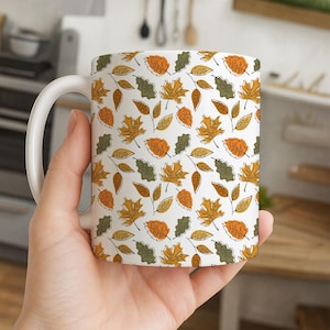 May include: White ceramic mug with a repeating pattern of autumn leaves in shades of orange, green, and brown. The leaves have the text "FUCK TRUMP" on them. The mug has a white handle.