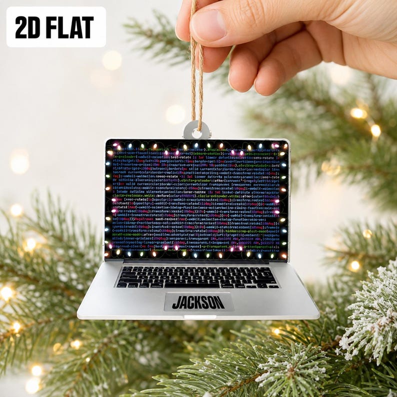 May include: A flat, laptop-shaped Christmas ornament featuring a screen displaying colorful lines of computer code framed by small, glowing holiday lights. The silver-colored laptop base includes a black trackpad with the name JACKSON printed.