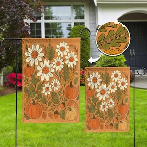 May include: A rectangular garden flag featuring an orange background with a pattern of white daisies, green leaves, and orange pumpkins. The text "Fuck Trump" is printed in a cursive font among the foliage. The design is displayed on two flags.