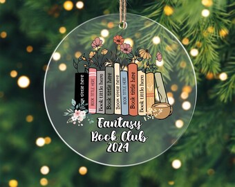 May include: A clear, round ornament with a string for hanging. The ornament features a stack of books with the text "Book tittle here" and "Fantasy Book Club 2024". Colorful flowers and a coffee cup are also depicted.