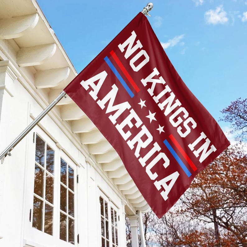 Puede incluir: Una bandera roja con texto blanco que dice "NO KINGS IN AMERICA" con tres estrellas blancas y dos rayas rojas y azules.