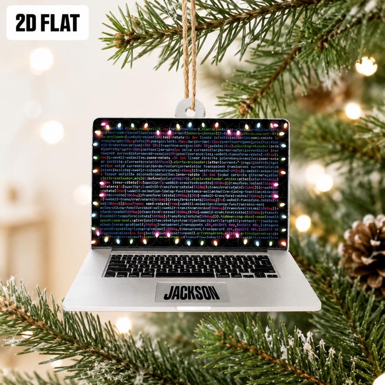 May include: A flat, silver-colored laptop ornament featuring a screen display of dense computer code framed by colorful Christmas lights. The name JACKSON is printed in black on the palm rest area. The ornament hangs from a tan twine loop.