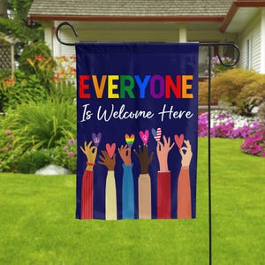 May include: A navy blue garden flag with the text "EVERYONE Is Welcome Here" in rainbow colors. The flag features illustrations of hands holding hearts and symbols of peace, love, and unity.