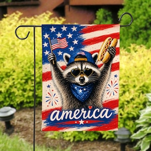 May include: A rectangular garden flag featuring a raccoon wearing a blue baseball cap, heart-shaped sunglasses, and a blue bandana. The raccoon holds a small American flag and a hot dog. The background displays the American flag with the word america.