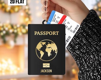 May include: Black passport-shaped ornament with gold world map and text "PASSPORT" and "JACKSON". A boarding pass is tucked behind it. The ornament is held by a string.