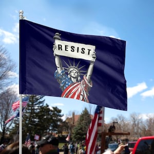 May include: A blue flag with a white background featuring a depiction of the Statue of Liberty holding a sign that reads "RESIST".