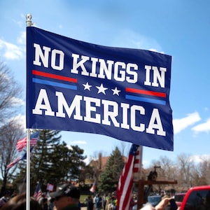 Puede incluir: Una bandera azul con texto blanco que dice "NO KINGS IN AMERICA". La bandera tiene tres estrellas blancas y rayas rojas y azules.
