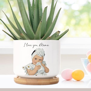 May include: White ceramic planter with a bamboo base. The planter features a hand-drawn illustration of a baby girl holding a bottle. The text "I love you, Mama" is printed on the planter.