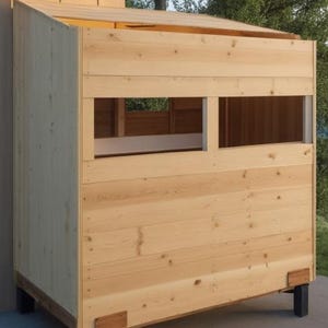 Op de afbeelding: Een houten constructie met een schuin dak en twee rechthoekige ramen. De constructie is gemaakt van lichtgekleurd hout en staat op zwarte metalen poten. De ramen bieden uitzicht naar buiten.