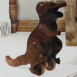 May include: A wooden toy dinosaur with wheels. The dinosaur is brown and has a long tail. The wheels are black and have a metal axle.